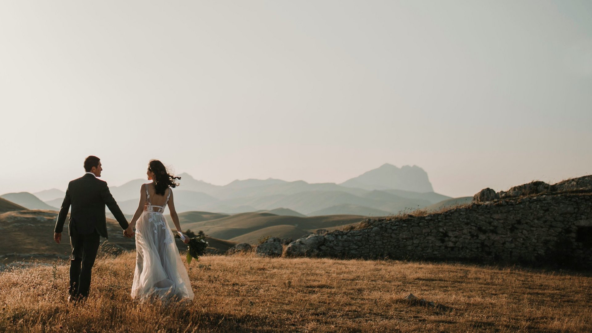 Hochzeitslocation in Tirol: ADEA Lifestyle Suites Paar in Hochzeitskleidung hält sich an der Hand auf einem Hügel bei Sonnenuntergang