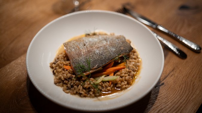 ADEA Lifestyle Suites – romantisches Hotel in Tirol Gebratenes Fischfilet auf Gerste und Gemüse in weißem Teller auf Holztisch