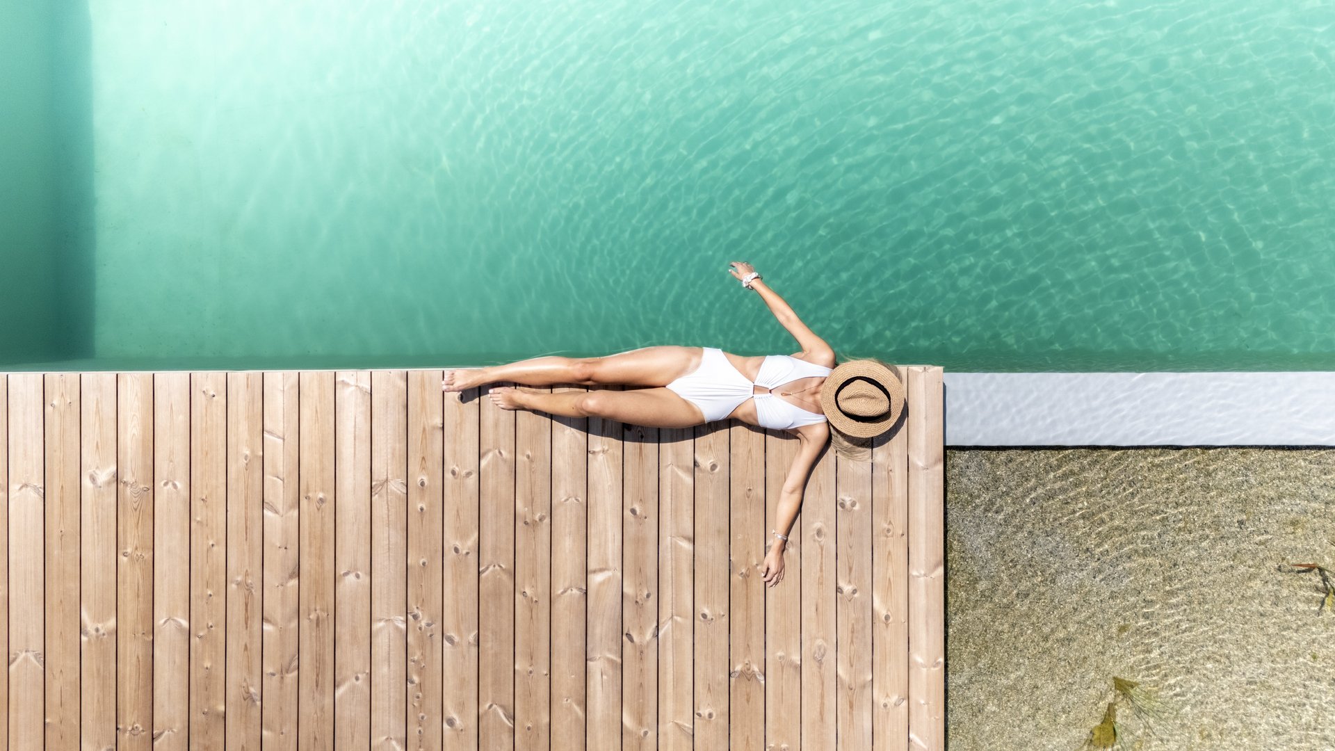 Holiday in Fieberbrunn at the ADEA Lifestyle Suites Woman in white swimsuit with straw hat relaxing on wooden dock by pool