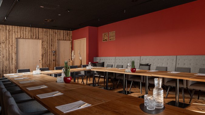 Meetings im Seminarhotel in Tirol Moderner Besprechungsraum mit Holz- und roten Wänden, Stühlen und Tisch mit Glaskaraffen