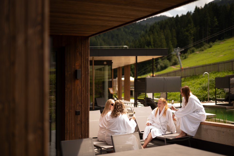Freundinnen sitzen gemeinsam im Bademantel auf der Terrasse und genießen ein Getränk Freundinnen sitzen gemeinsam im Bademantel auf der Terrasse und genießen ein Getränk
