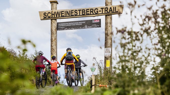 Familie beim Downhillen unter dem Schild Schweinestberg-Trail in Fieberbrunn Familie beim Downhillen unter dem Schild Schweinestberg-Trail in Fieberbrunn
