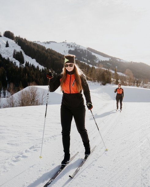 Urlaub für... Zwei Frauen beim Langlaufen im Schnee vor bewaldeten Bergen