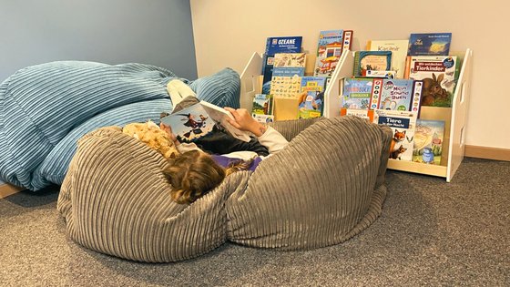 Urlaub für... Kind liest Buch auf grauem Sitzsack neben blauem Sitzsack und Bücherregal