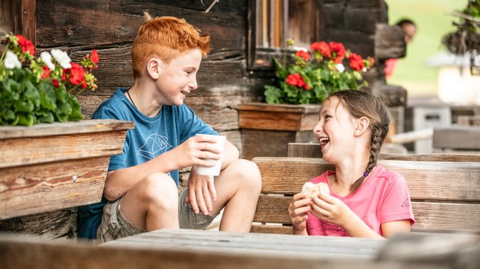 Zwei lachende Kinder sitzen draußen vor einer Almhütte Zwei lachende Kinder sitzen draußen vor einer Almhütte