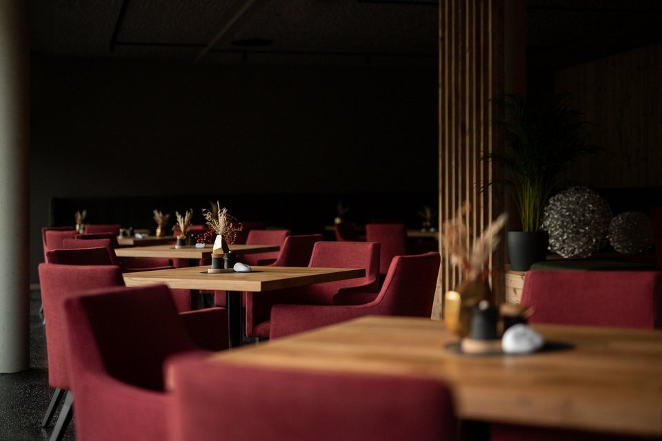 Hochzeitslocation in Tirol: ADEA Lifestyle Suites Leeres Restaurant mit roten Stühlen und Holztischen in gedämpftem Licht