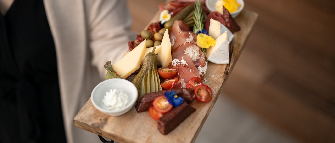 Brettljause mit Speck, Schinken und Käse wird auf einem Holzbrett serviert Brettljause mit Speck, Schinken und Käse wird auf einem Holzbrett serviert