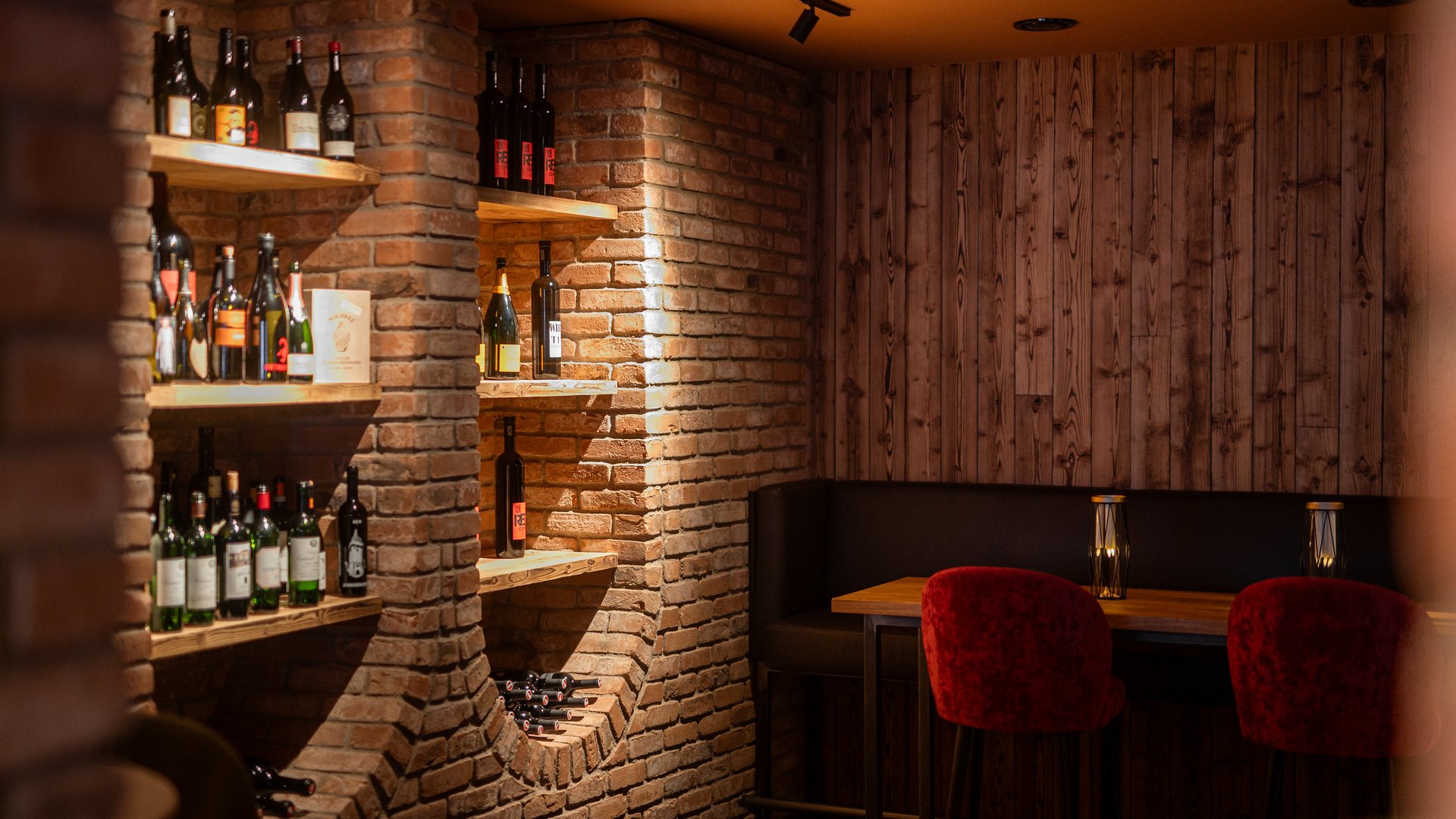 Weinlounge mit Sitzmöglichkeiten und roten Stühlen und einem gefüllten Weinregal Weinlounge mit Sitzmöglichkeiten und roten Stühlen und einem gefüllten Weinregal