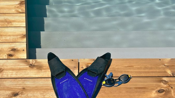 Blaue Schwimmflossen und Schwimmbrille liegen auf dem Steg vor dem Schwimmteich Blaue Schwimmflossen und Schwimmbrille liegen auf dem Steg vor dem Schwimmteich