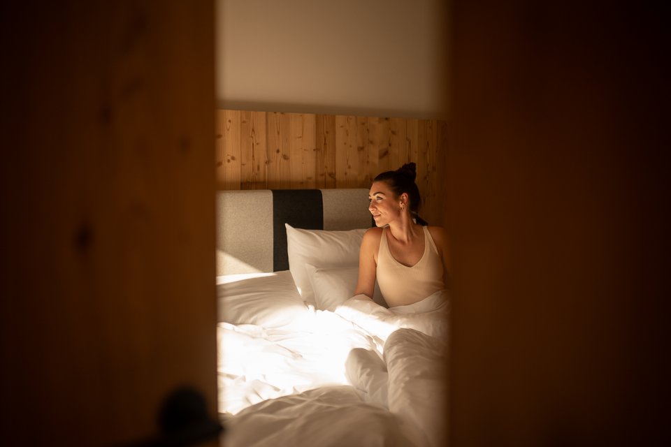 ADEA Lifestyle Suites: dein Hotel mit Sauna im Zimmer in Tirol Frau sitzt im Bett und schaut entspannt aus einem Holzrahmen