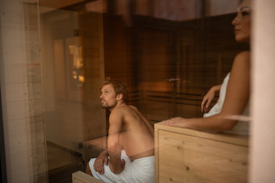 ADEA: dein Hotel mit Fitnessstudio in Österreich Mann und Frau entspannen in einer Sauna mit Holzvertäfelung