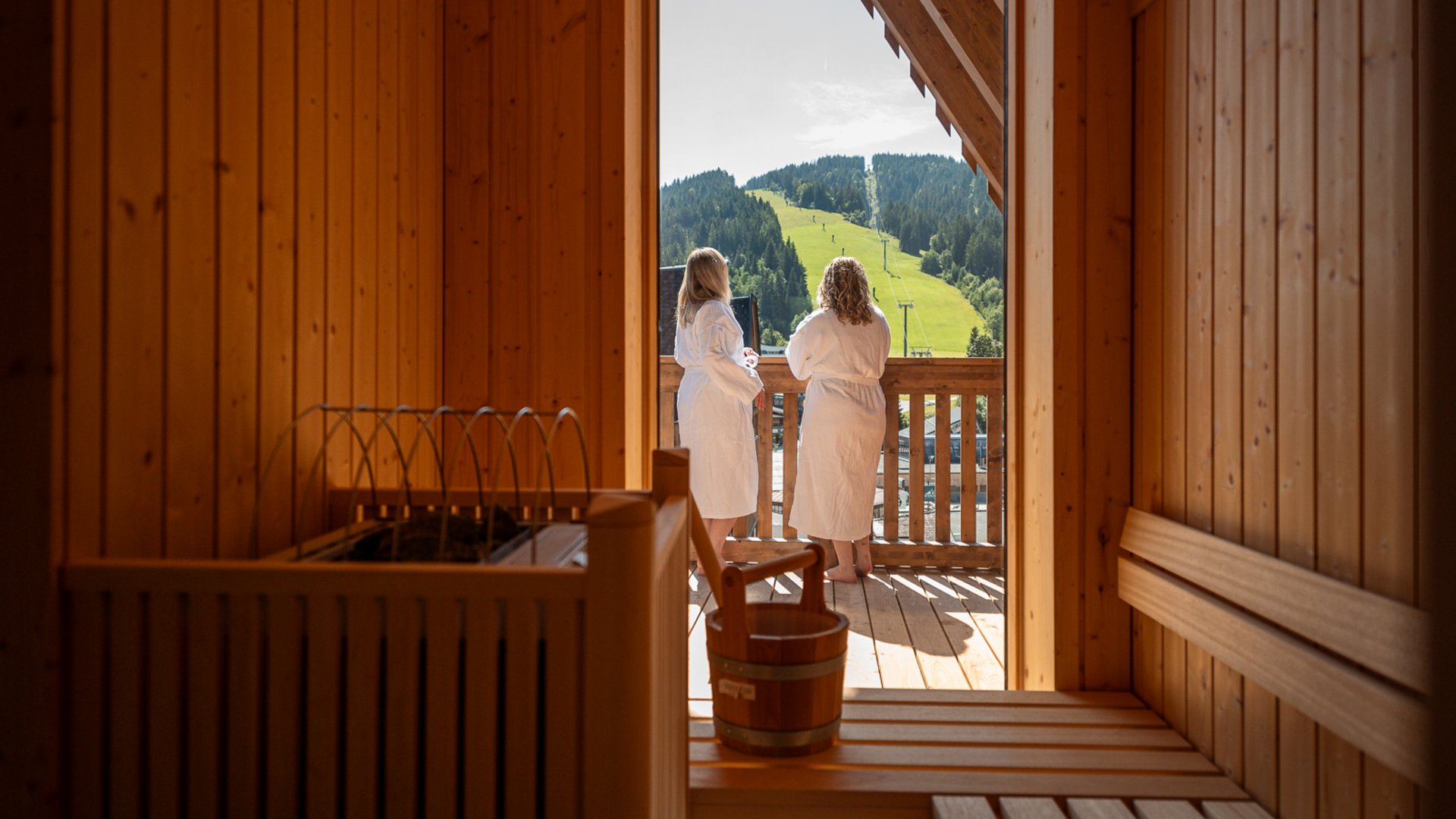 ADEA Lifestyle Suites: dein Hotel mit Sauna im Zimmer in Tirol Zwei Frauen in Bademänteln stehen auf dem Balkon einer Sauna mit Bergblick.