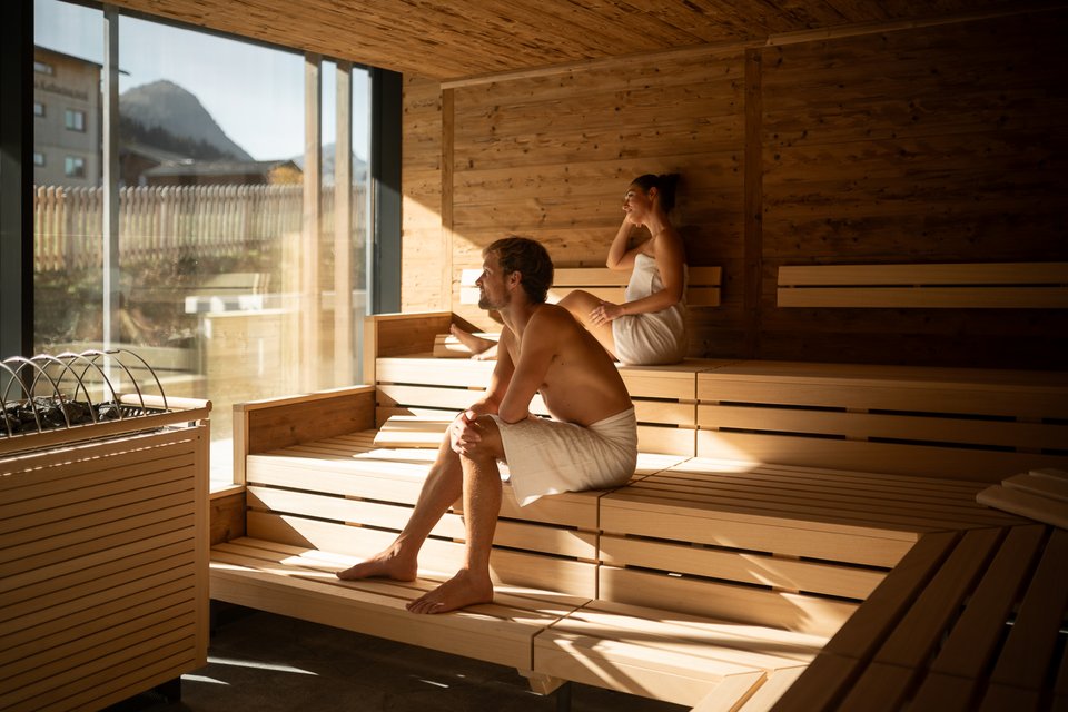 Paar sitzt in Panoramasauna mit Bergblick Paar sitzt in Panoramasauna mit Bergblick