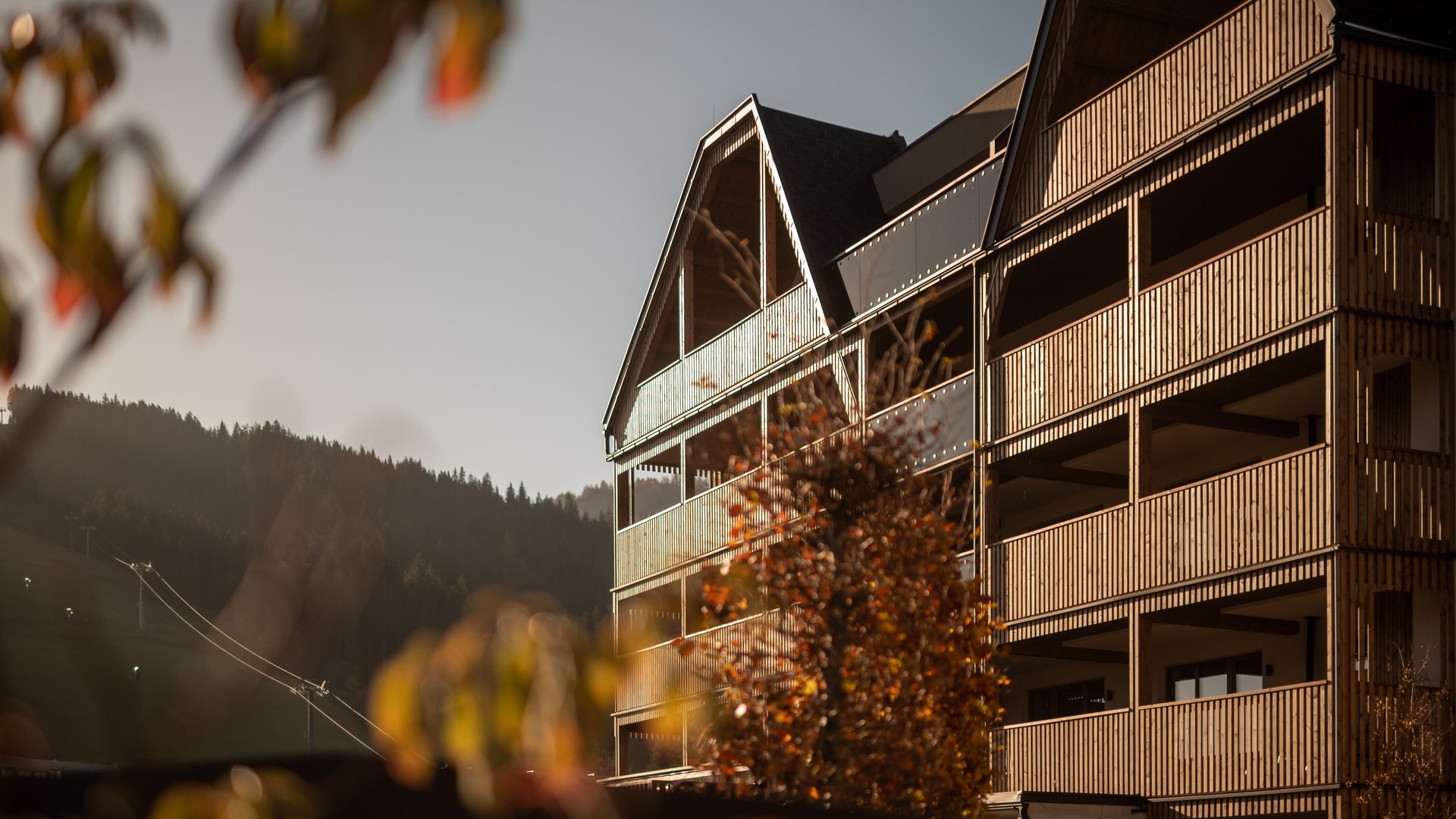 Hotel in Fieberbrunn: ADEA Lifestyle Suites Holzhaus mit Balkon im Herbst bei Sonnenlicht vor Berglandschaft