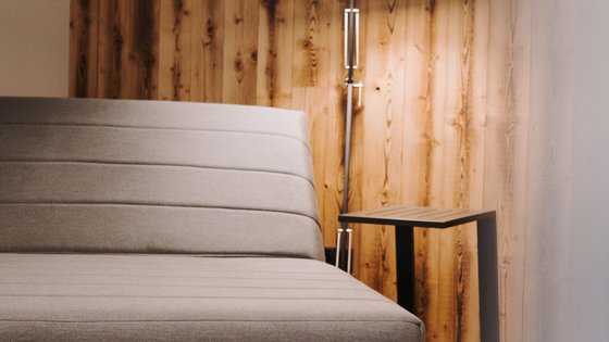 Fieberbrunn: Wellnesshotel gesucht? Graues Sofa vor einer Holzpaneelwand mit Stehlampe und kleinem Tisch