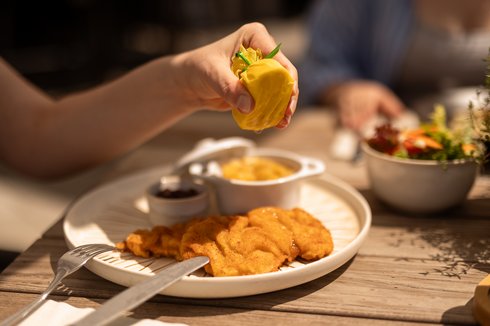 Fieberbrunn: Wellnesshotel gesucht? Hand presst Zitrone über Wiener Schnitzel mit Beilagen auf Teller
