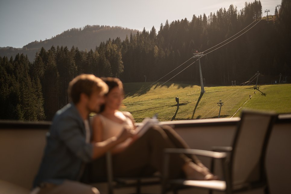 Hotel in Fieberbrunn: ADEA Lifestyle Suites Paar sitzt auf einem Balkon mit Blick auf die Kitzbüheler Alpen und liest gemeinsam