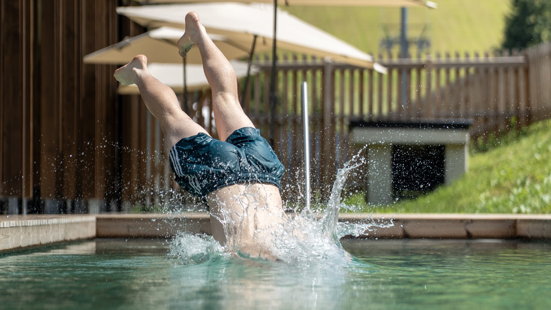Fieberbrunn: Wellnesshotel gesucht? Person taucht kopfüber in einen Pool mit Bergwiese im Hintergrund