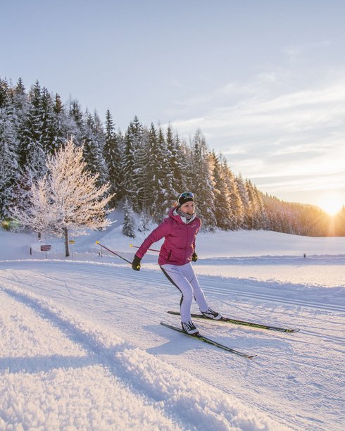 Hotel in Fieberbrunn: ADEA Lifestyle Suites Langläuferin in roter Jacke im verschneiten Wald bei Sonnenaufgang