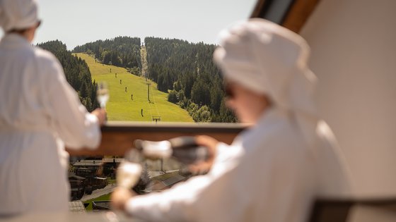 Hotel in Fieberbrunn: ADEA Lifestyle Suites Zwei Personen in Bademänteln mit Tüchern auf dem Kopf genießen einen Bergblick vom Balkon