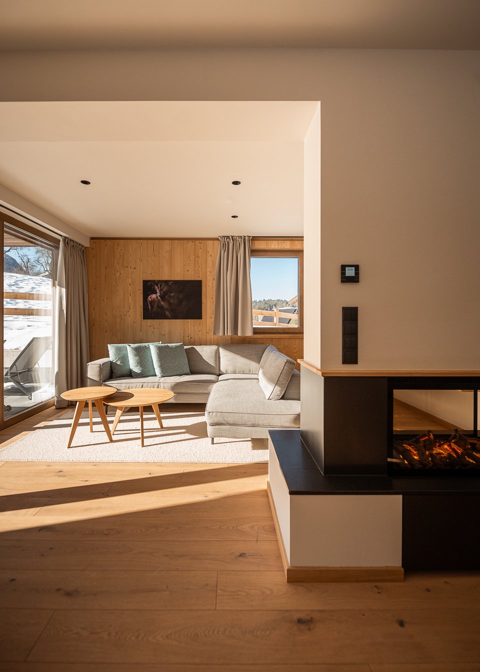 Hotel in Fieberbrunn: ADEA Lifestyle Suites Hell eingerichtetes Wohnzimmer mit grauer Eckcouch und modernem Kamin